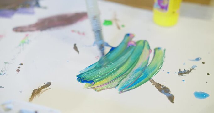 Close-up of a brush mixing vibrant paint on white paper, capturing the messy, tactile process of creative expression and childhood art therapy activity.