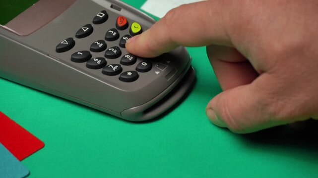 Hand pressing buttons on a payment terminal with colorful cards on a green surface, illustrating the transaction process in a retail setting