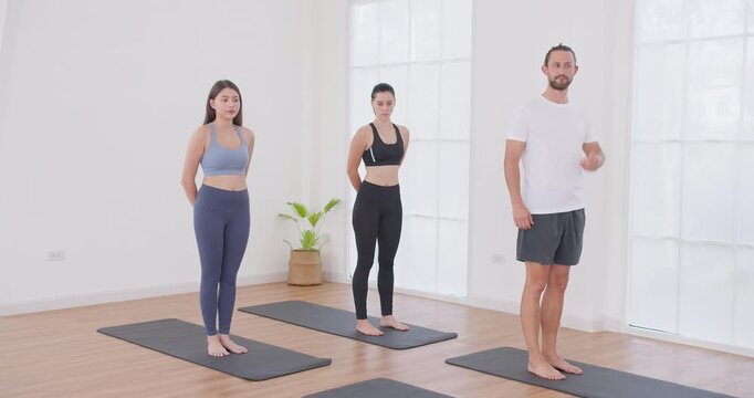 A diverse group practices a grounding pose on yoga mats in a bright studio, focusing on mindfulness and physical alignment during a group wellness class.