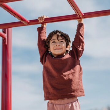 Child hanging from red monkey bars at outdoor playground