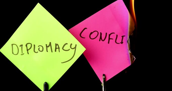 A sticky note with conflict word burns until it turns to ash while diplomacy note stays safe on a black background. Symbol of peace and resolution.