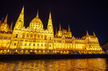 Obraz premium Illuminated Hungarian Parliament Building at Night by the Danube River in Budapest, Hungary; Magnificent Gothic Revival Architecture and Golden City Skyline Reflection on Water