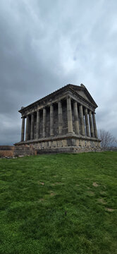 The Garni Temple in Armenia, a classical structure with columns, stands on a grassy hill under an overcast sky. The ancient edifice features a triangular pediment