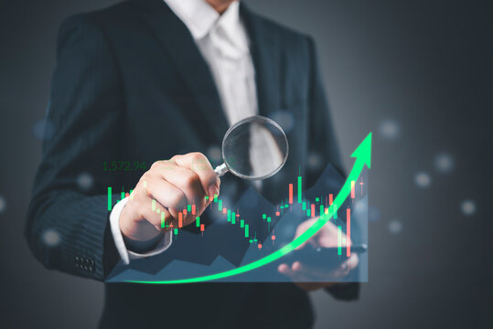 Close up hand holding magnifying glass scrutinizing financial growth chart candlestick patterns stock market forecast investment strategy data visualization.