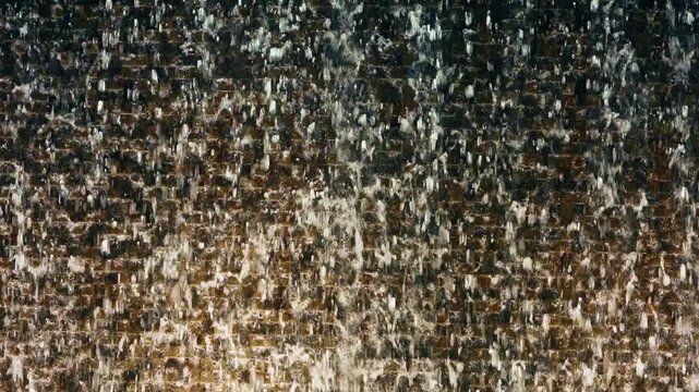 Water streams cascade down a dark textured stone wall creating a mesmerizing water feature display in Dubai. Droplets splash against brown and black tiles forming beautiful patterns.