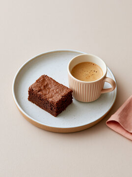 Dark chocolate brownie with espresso in a pink ribbed mug on a speckled plate in a minimalist dessert scene.