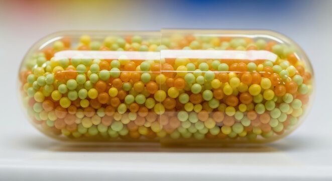Capsule filled with colorful tiny pellets sits against a clean white background.