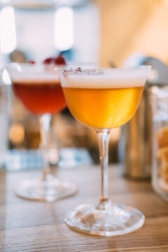 Frothy cocktail. Aperitif glass. Mixed drink served on metal tray. Bar liquid with whipped white top dried flower petals aromatic garnish.