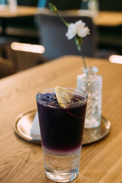 Cold cocktail. Purple drink. Glass with dark color layered alcohol shot served with ice lemon slice garnish on restaurant table.