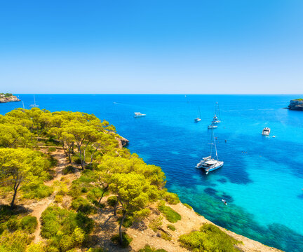 Aerial view of luxury yachts and boats anchored in a turquoise bay with crystal clear water on the coast of Mallorca, Spain. Scenic Mediterranean landscape during a bright sunny summer day.