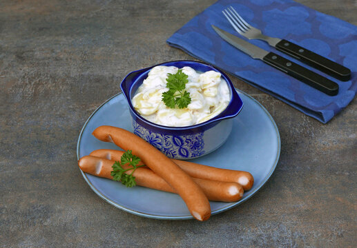 Vienna sausages with creamy potato salad in a ceramic bowl on a blue plate.