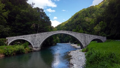 Fototapeta premium Old Stone Arch Bridge Over A Serene River In A Lush Green Valley.