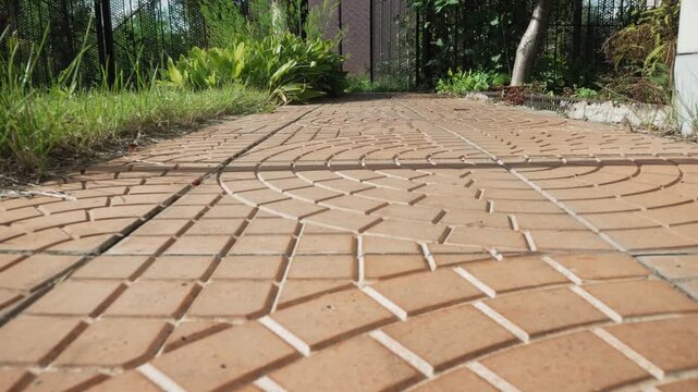 Macro closeup terracotta tile pathway, lowangle perspective revealing circular brick pattern, sunlight casting soft shadows across textured surface, grass and garden border blurred in background, warm
