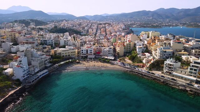 Greece Crete Agios Nikolaos 4K Drone Side View of Small Town Beach and Marina with Colorful Houses by the Sea Scenic Coastal Panorama and Turquoise Water Travel