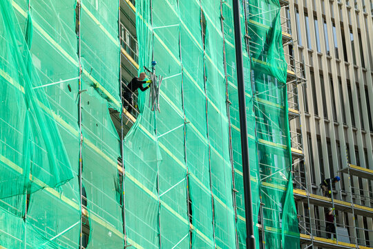 Workers on scaffolding at construction site covering building with green netting