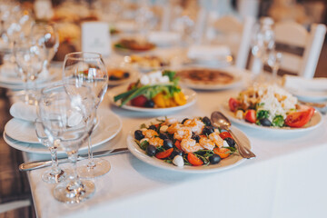Fototapeta premium A table is set with various plates of food including seafood salad and other dishes. Glasses of water and wine are placed around the table. The setting is busy with people dining and talking
