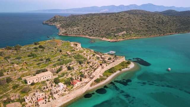 Spinalonga Island Crete Greece 4k aerial drone view of Venetian fortress and leper colony ruins. Turquoise sea of Plaka bay with tourist boat and historic stone walls. Famous Greek travel landmark