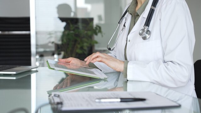 Doctor woman accessing patient data on digital tablet, managing healthcare records in modern medical office. Medicine, health care and science concept