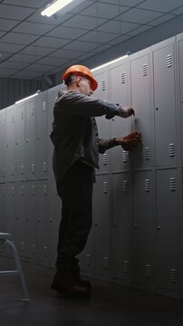 Group of Blue Collar Professionals in Orange Safety Helmets Talking and Opening Metal Lockers in Clean Industrial Dressing Room After Finishing Duty. Teamwork and Work Life Balance. Vertical Shot.