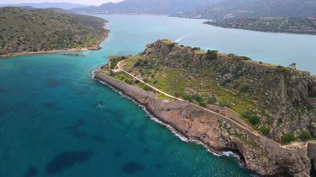 Aerial view of Spinalonga Island fortress in Crete, Greece. Drone flight over Venetian castle walls with tourist boats in turquoise water and emerald sea. Historic landmark in Elounda bay 4k.