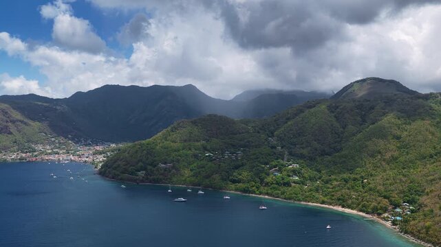 Aerial drone footage of the majestic Piton mountains rising above lush tropical rainforest and turquoise Caribbean waters in Saint Lucia with sailboats anchored in the bay and colorful coastal town.