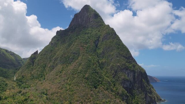 Aerial footage reveals the majestic Piton volcanic peaks covered in lush tropical rainforest rising dramatically from the deep blue Caribbean Sea in Saint Lucia with boats below.