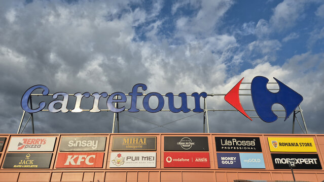 A large outdoor Carrefour retail sign set against a cloudy sky, featuring various smaller shop logos beneath it. Picture taken on May 2, 2026 in Ploiesti, Romania.
