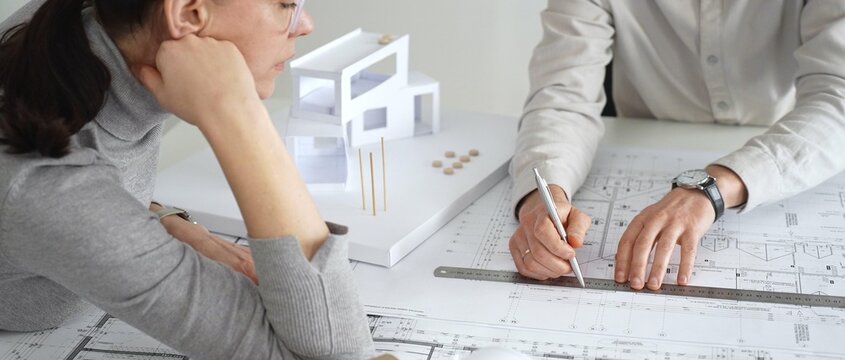 Architects engaging in a design planning meeting, analyzing blueprints and a scale model, making precise measurements and discussing new construction project ideas, close up