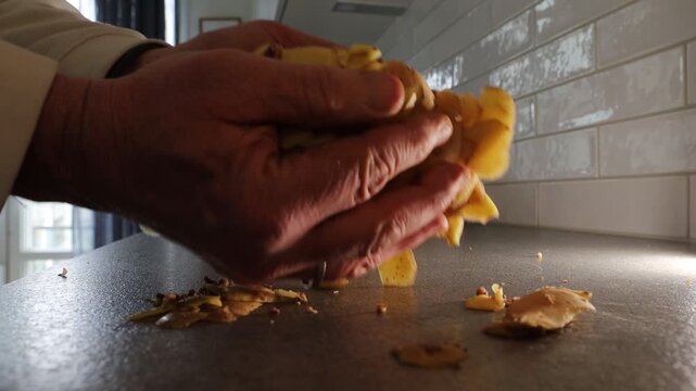 Stockholm, Sweden A cook in a residential kitchen takes fresh potato peels with his hands and places them into a brown paper recyclable bag for composting.  