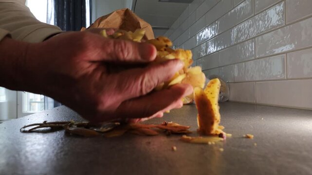 Stockholm, Sweden A cook in a residential kitchen takes fresh potato peels with his hands and places them into a brown paper recyclable bag for composting.  