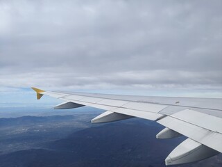 Obraz premium View from airplane window showing wing over mountains and clouds during flight