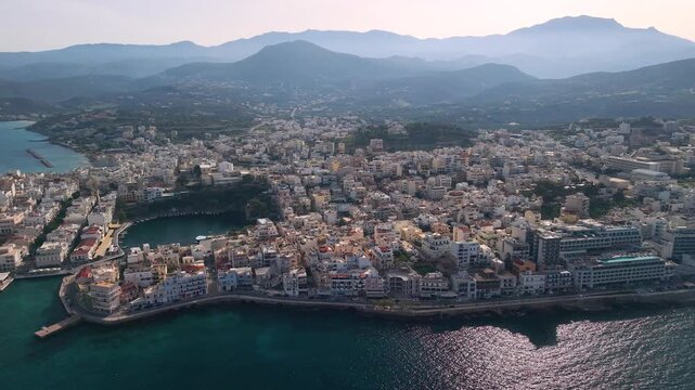 Agios Nikolaos Crete Greece 4k aerial drone pan of Voulismeni Lake and city skyline. Scenic sunset view of coastal town harbor and old architecture in Mirabello Bay. Beautiful Mediterranean travel