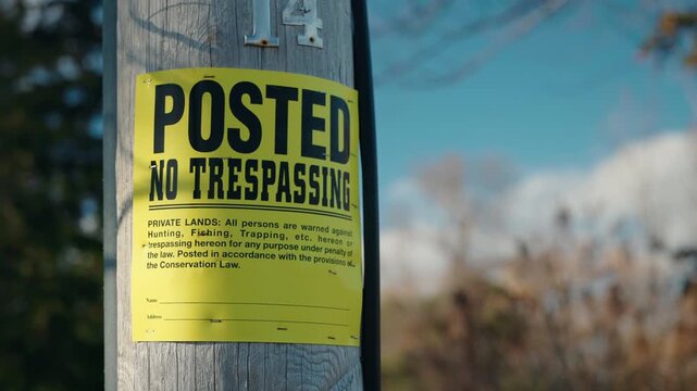 Yellow posted no trespassing sign on wooden pole, warning of private property and restricted access outdoors