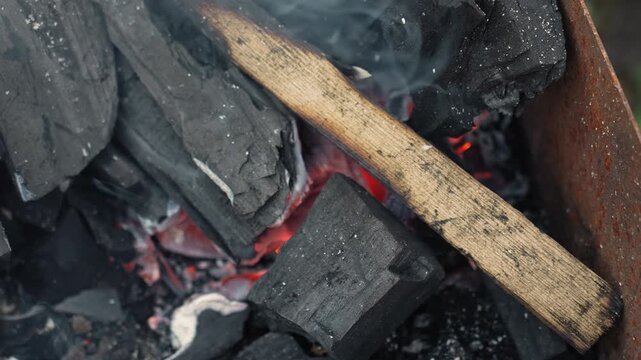 Macro closeup glowing charcoal and ember, ash dust swirling, small wooden stick resting over hot coals, slow smoke trails, meditative backyard grill scene suggesting camp chef, artisan blacksmith