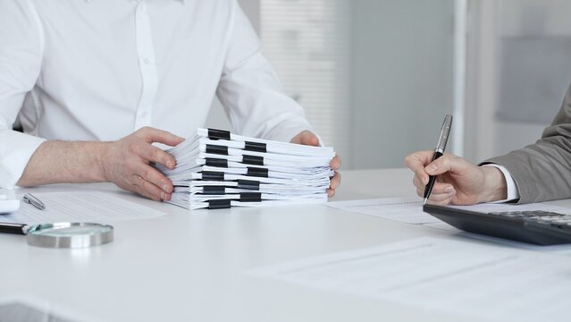 Professionals handling a large stack of documents and paperwork, signing a contract in a busy office. Audit and taxes in business