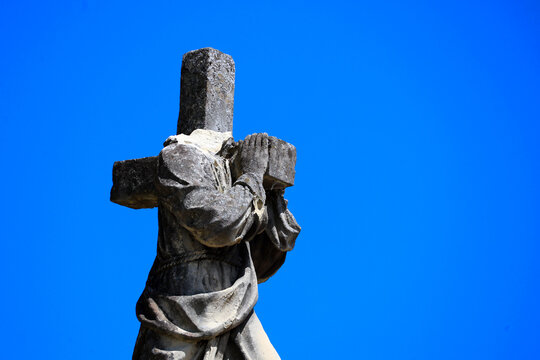damaged, headless stone statue of Jesus carrying the cross against a blue sky