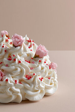Studio shot of decorated cake slice with whipped cream, sprinkles and pink flowers on a beige background.