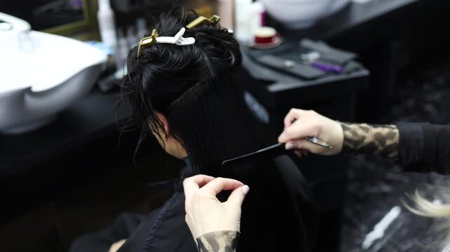 Close-up of a hairdresser holding a hairdresser scissors and a comb and cutting woman's hair at beauty salon