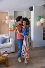 Naklejka premium Two women hugging and posing in living room with HAPPY banner, balloons, sash near white sofa