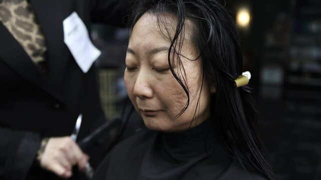 Beautiful Asian woman getting haircut in beauty salon, professional hairdresser cutting long black hair with scissors. Trendy hairstyle, self care and confidence concept.