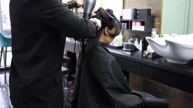 Beautiful Asian woman getting haircut in beauty salon, professional hairdresser cutting long black hair with scissors. Trendy hairstyle, self care and confidence concept.