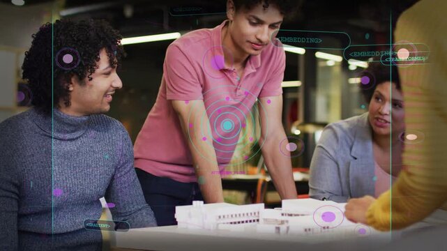 Design team reviewing scale model, seated man tapping model causing AR nodes highlighting elements