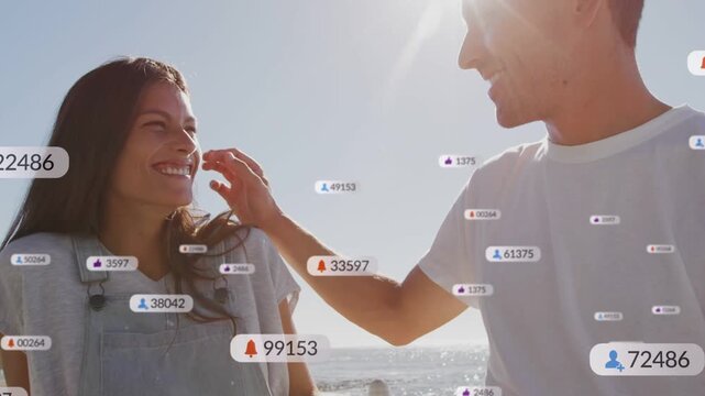 Couple seaside, social media bubbles appearing between them, man reaching brushing hair affection