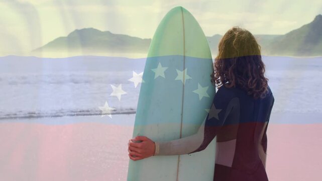 Woman surfer standing beach, holding board, scouting surf, turning head right under faint flag over