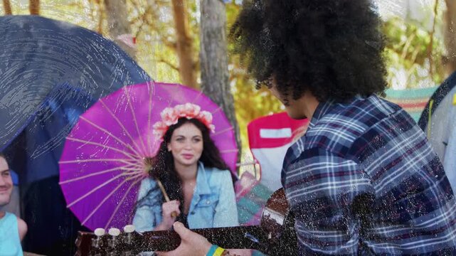 Guitarist strumming guitar in camp, animating music notes toward parasol listener, engaging friends
