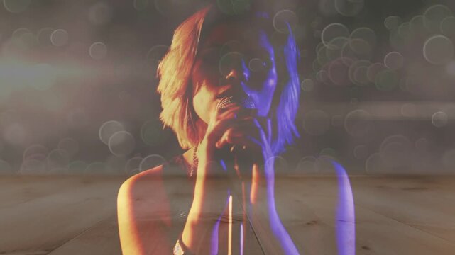 Camera revealing female singer moving hands up and singing into mic to perform music, bokeh rising