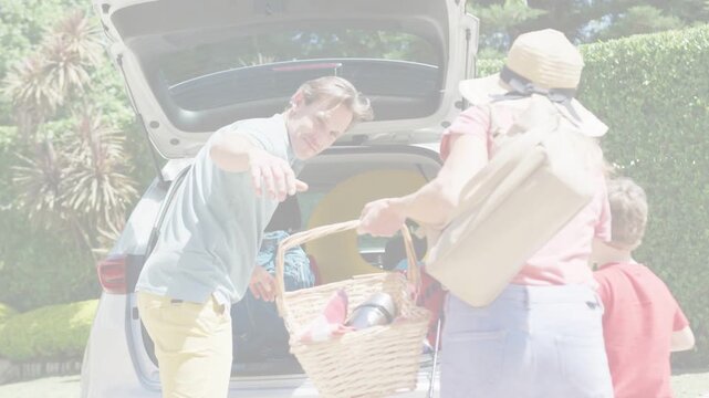 Family approaching SUV trunk, woman offering picnic basket, man sorting bags preparing leisure trip