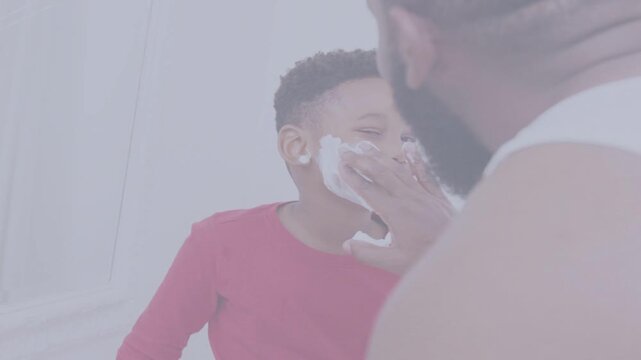 Father applying shaving foam to son in bathroom, reaching to teach playful hygiene routine