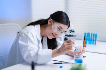 Female researcher pouring chemical liquid from a pipette into a beaker with blue solution, developing new medicine in a lab © amnaj
