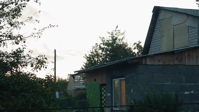 Macro close view dusk cottage rooftop, weathered cinderblock wall, corrugated metal roof, green wooden door, overgrown bushes, fading sunset light, rustic textures, quiet suburban garden, ideal